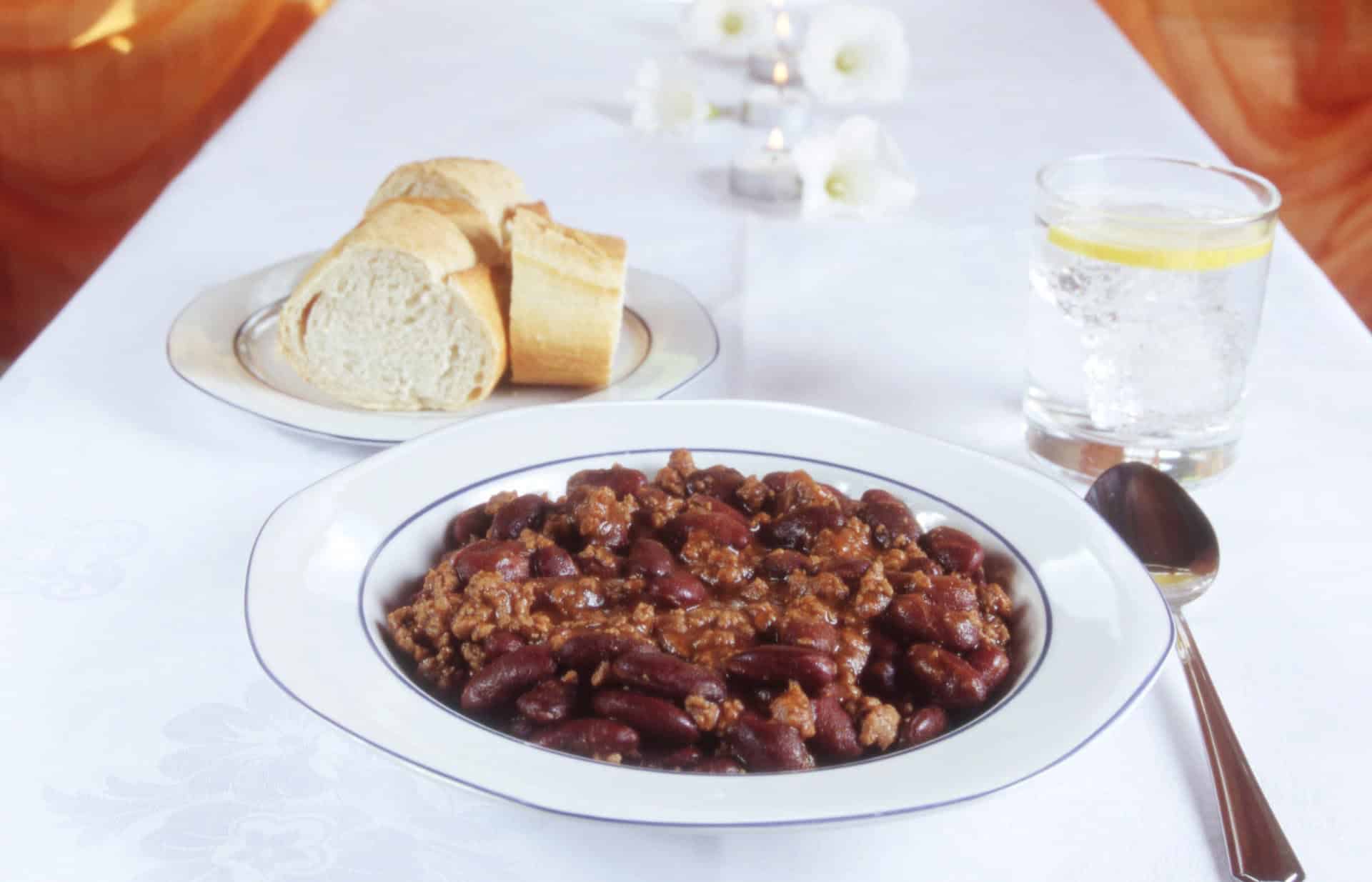 chili con carne på bordet med glas och bröd